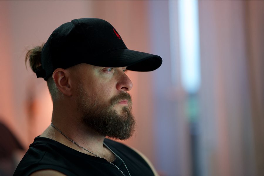 Luknar, a Czech artist and musician, in a black cap with his beard grown long, in profile against soft pink and blue studio light — the photograph as developed, with no look on it.