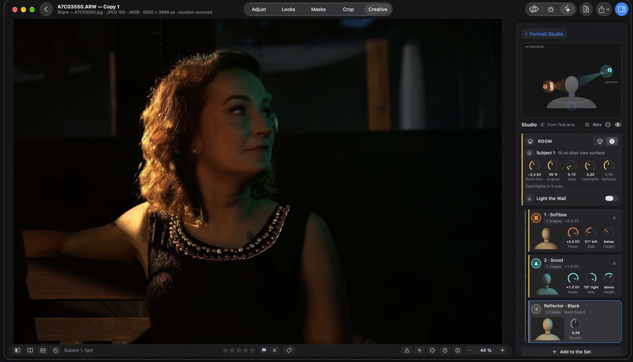Rebrilo on the Mac, the Portrait Studio on a red-haired woman sitting in a dark room: an orange light from the left catches her hair and cheek, a teal light from the right touches the far side, and the room around her is taken down to near black. On the right the plan of the room with the two lamps round a head, then the room controls with Light the Wall, and cards for a softbox, a snoot and a black reflector.